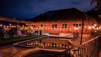 A pool area with lounge chairs and a thatched-roof building.