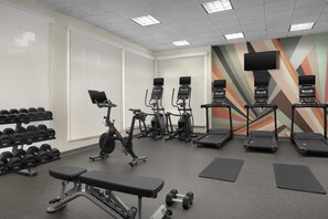 Un gimnasio con cintas de correr, elípticas, mancuernas y bancos.