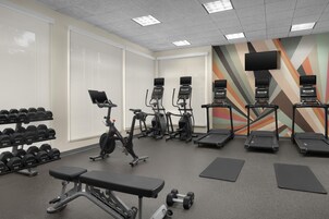 Un gimnasio con cintas de correr, elípticas, mancuernas y bancos.