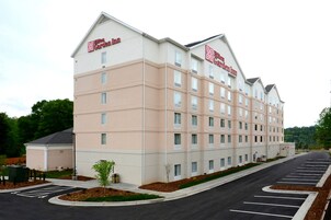 Un hotel de varios pisos con fachada color beige, múltiples ventanas y un estacionamiento con espacios delimitados.