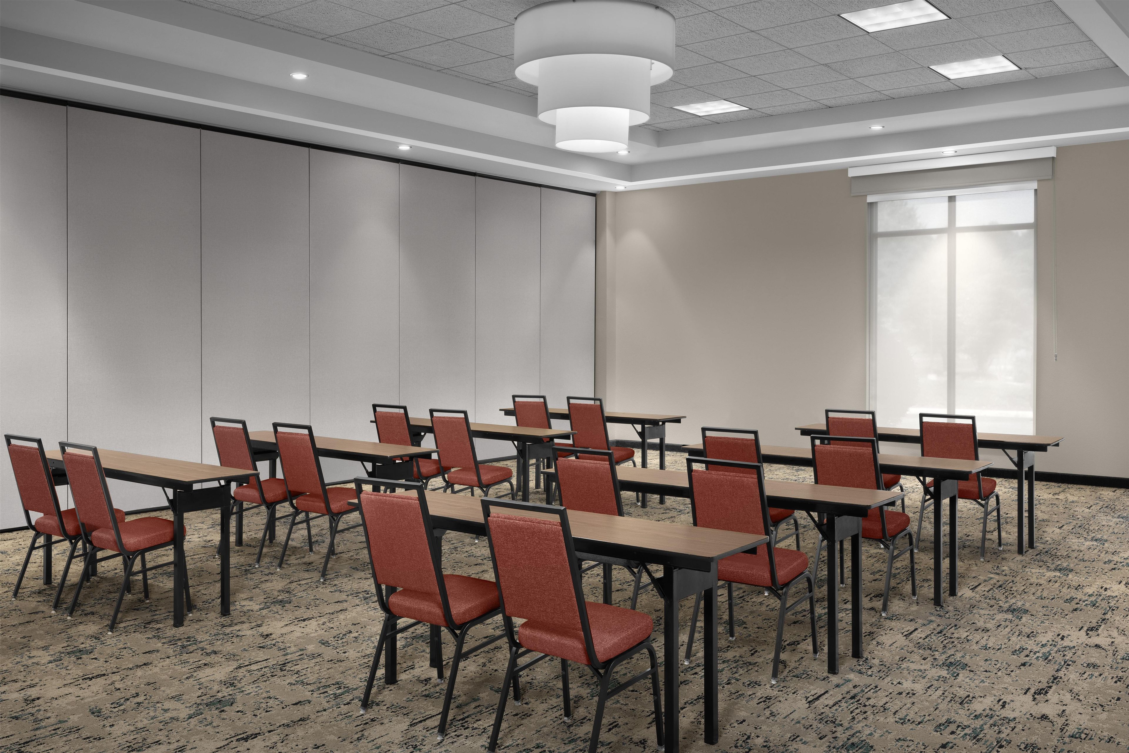 A conference room with tables and chairs, a large window, and a carpeted floor.