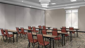 A conference room with tables and chairs, a large window, and a carpeted floor.