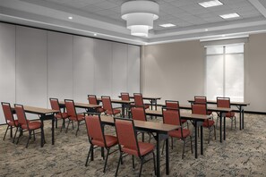 Ein Konferenzraum mit Tischen, Stühlen, einem großen Fenster und Teppichboden.