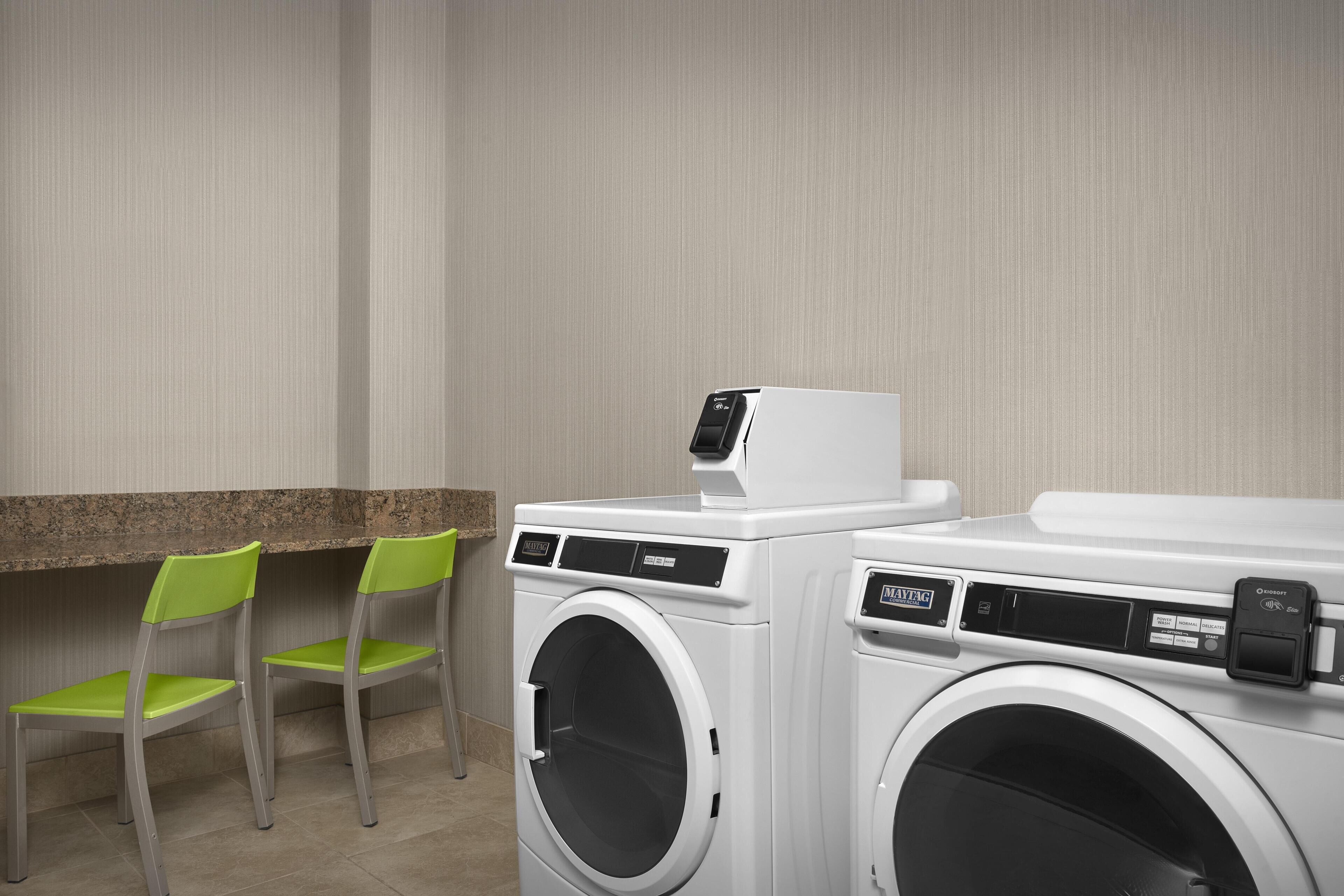 A laundry area with a washing machine, dryer, and two chairs.