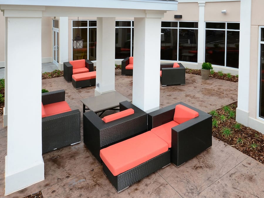 Een terras buiten met rieten meubels en oranje kussens.