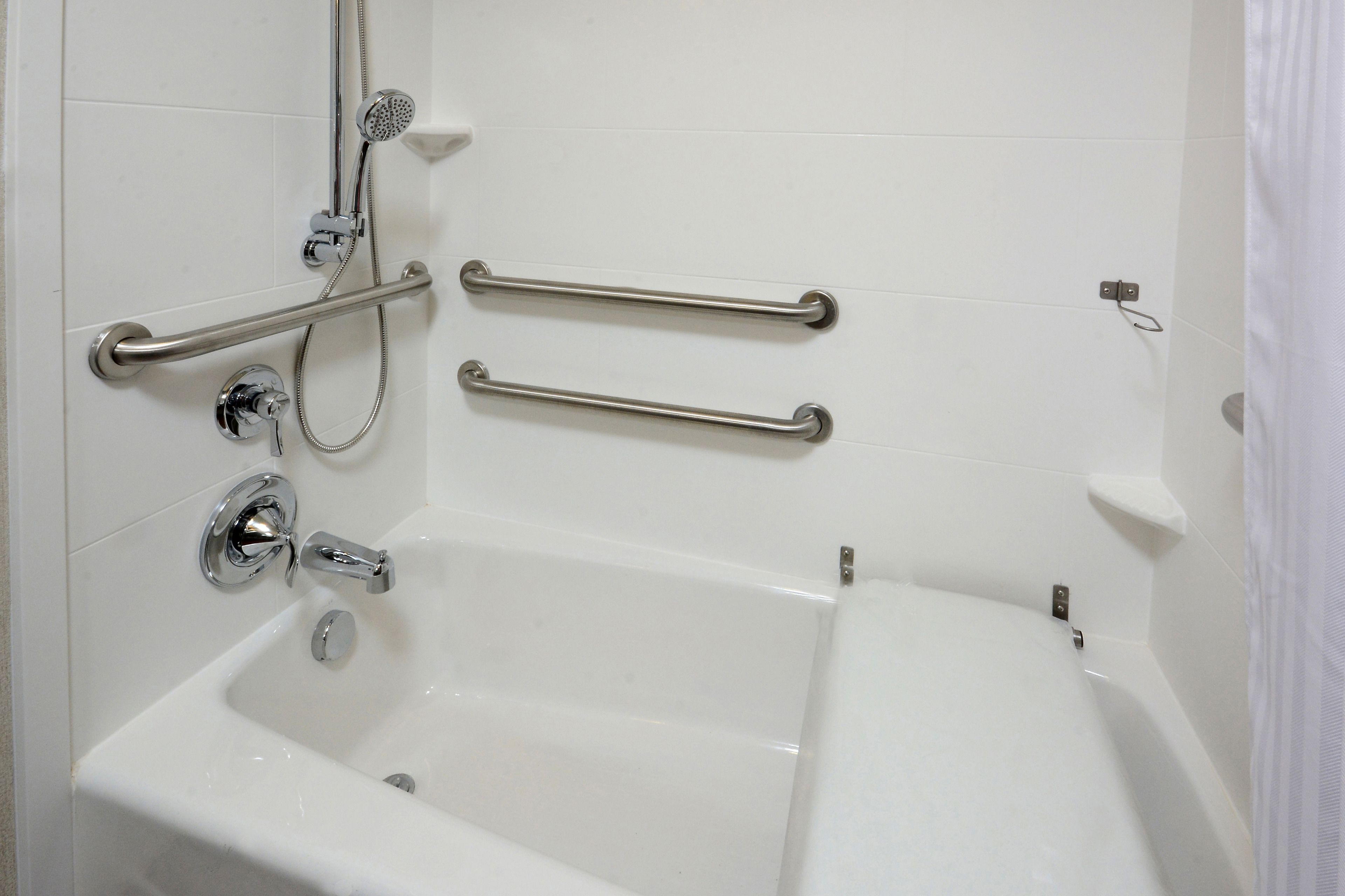 A bathroom with a bathtub, grab bars, and a shower head.