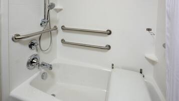 A bathroom with a bathtub, grab bars, and a shower head.