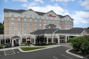 Un hotel de varios pisos con una entrada amplia, asientos al aire libre y un espacio reservado para personas con discapacidad.