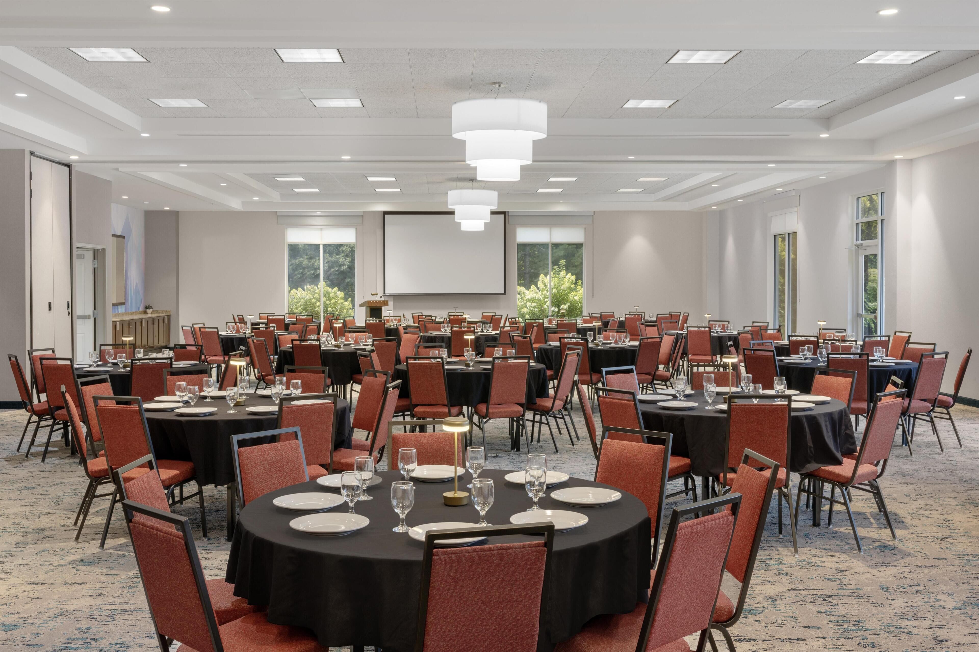 A large conference room with multiple round tables, each set with plates, glasses, and cutlery.