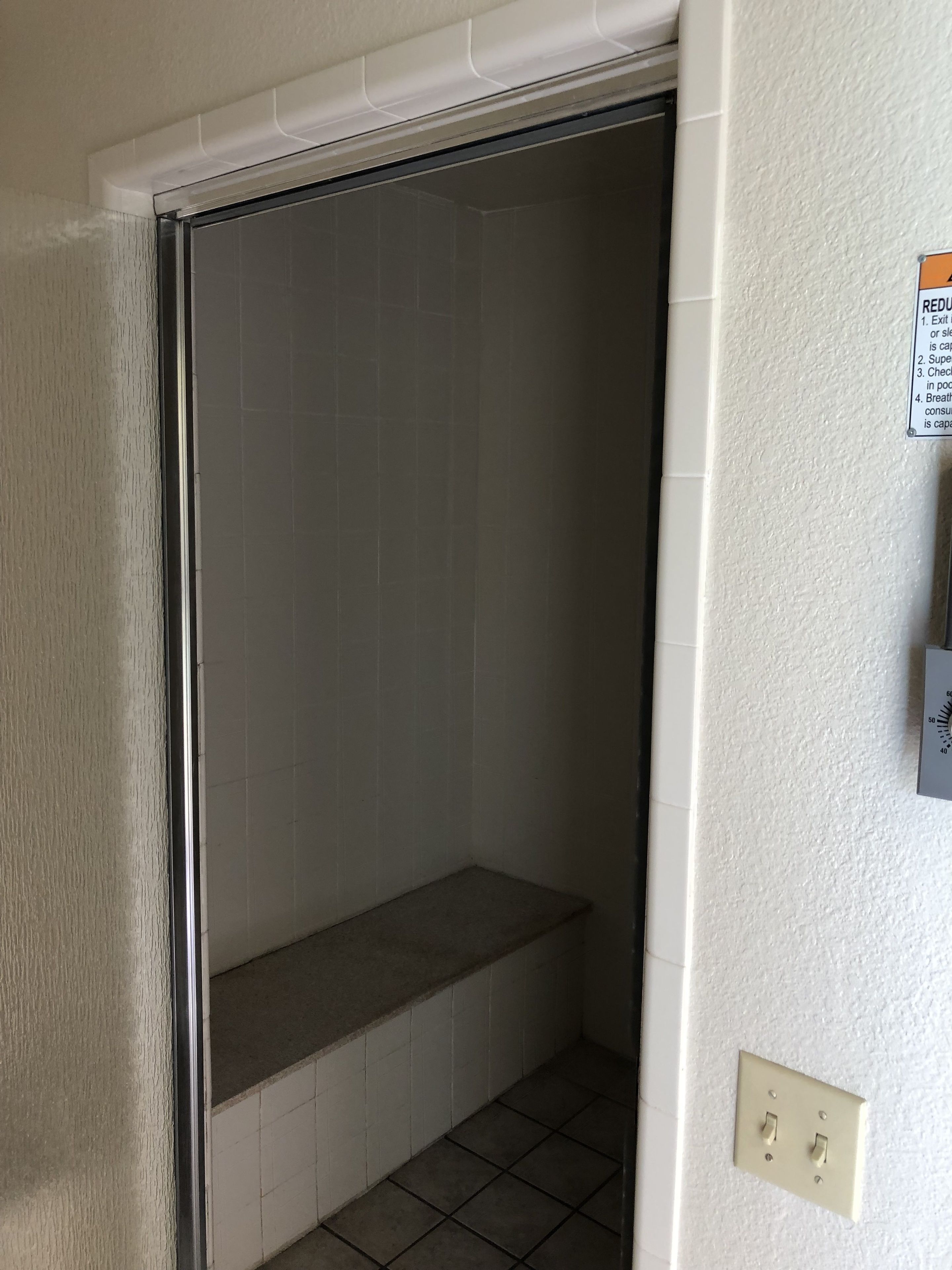 A bathroom with a shower stall, a towel rack, and a wall-mounted thermostat.