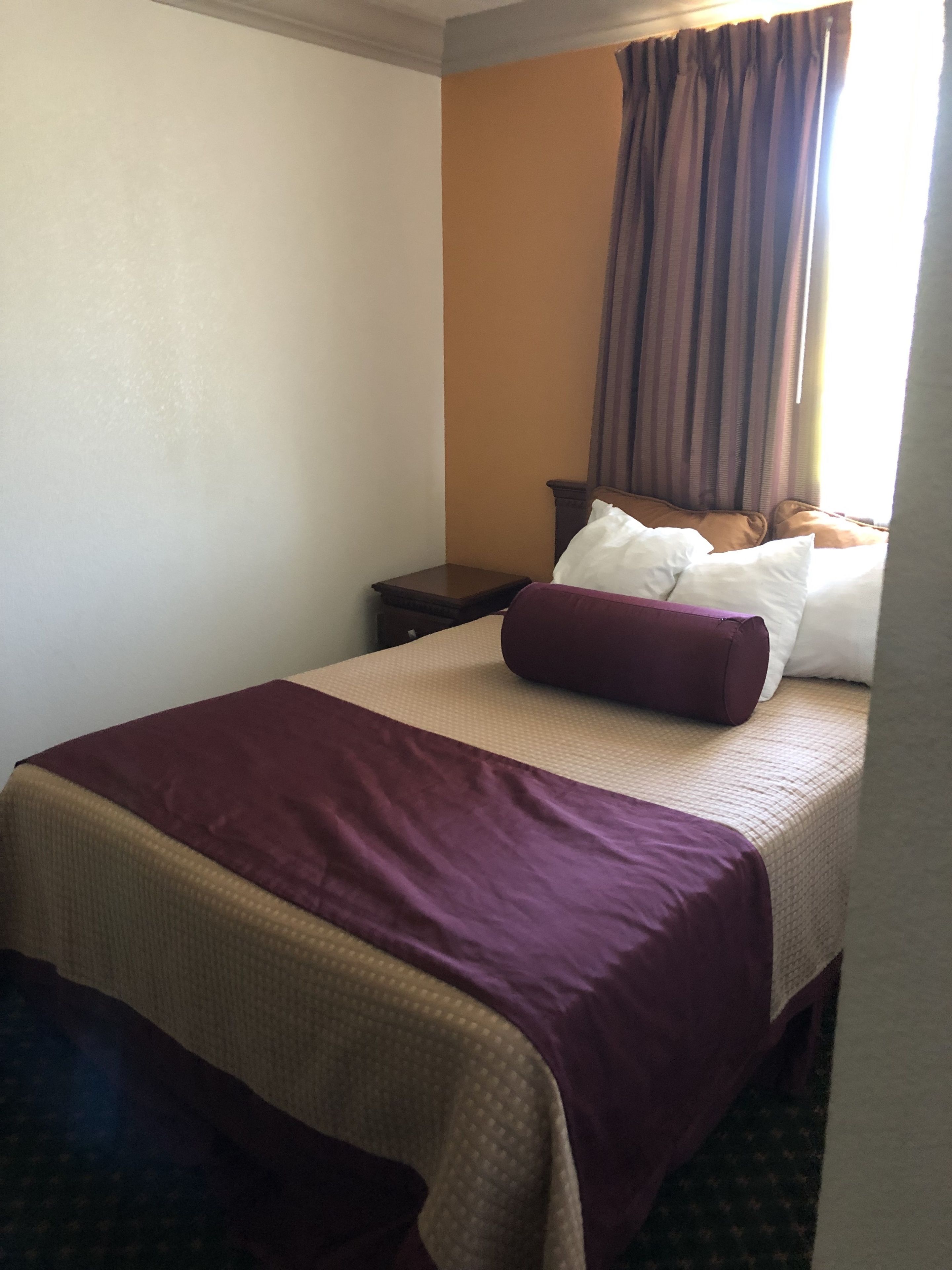 A hotel room with a bed, a nightstand, and a window with curtains.