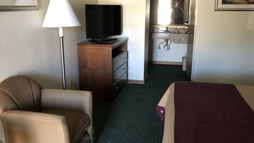 Une chambre d’hôtel avec un lit, une chaise, un bureau avec une lampe et un téléviseur.