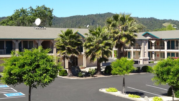 Un motel con estacionamiento, palmeras y montañas al fondo.
