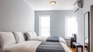 Habitación de hotel con dos camas, un escritorio y una silla. Hay dos ventanas con persianas, un equipo de aire acondicionado y un espejo en la pared.