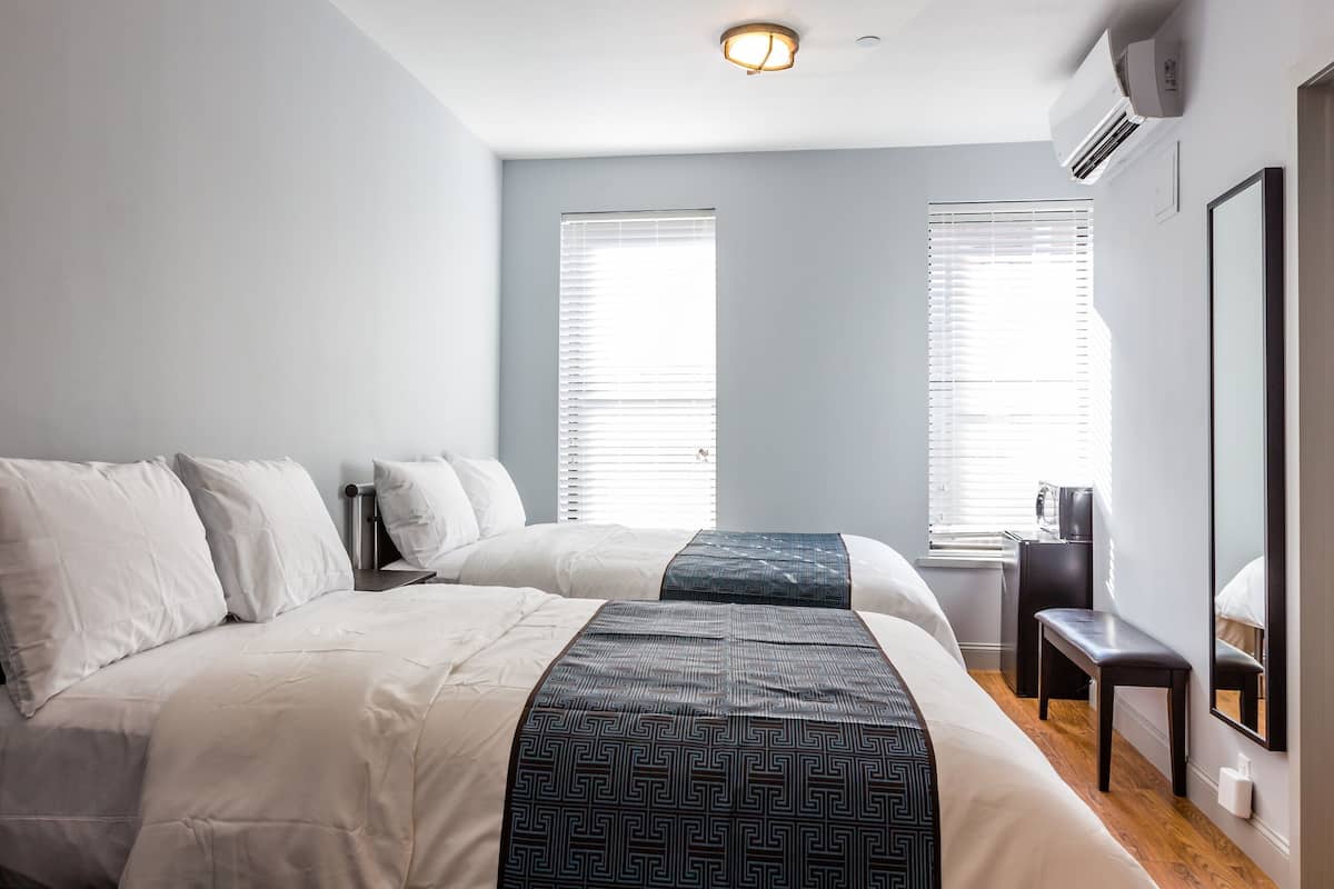 Hotelkamer met twee bedden, een bureau en een stoel. Twee ramen met jaloezieën, een airconditioning en een spiegel aan de muur.