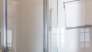 Un baño con ducha de mampara de vidrio, azulejos blancos y un inodoro blanco.