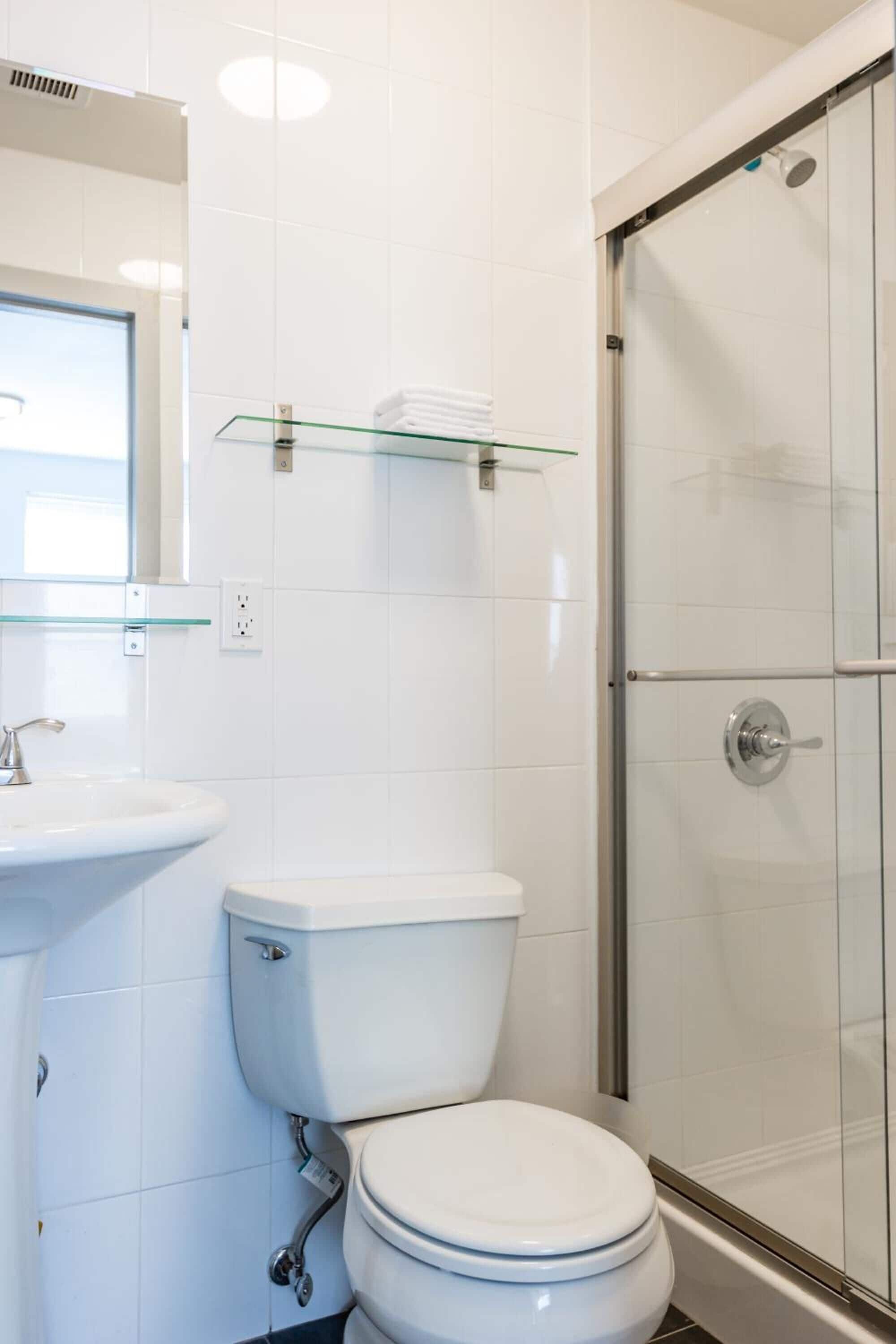 Un baño moderno con inodoro blanco, repisa de vidrio sobre el lavabo y cabina de ducha con puertas de vidrio.