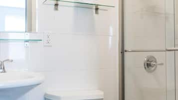 Un baño moderno con inodoro blanco, repisa de vidrio sobre el lavabo y cabina de ducha con puertas de vidrio.
