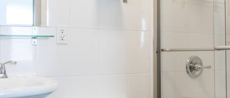 Un baño moderno con inodoro blanco, repisa de vidrio sobre el lavabo y cabina de ducha con puertas de vidrio.