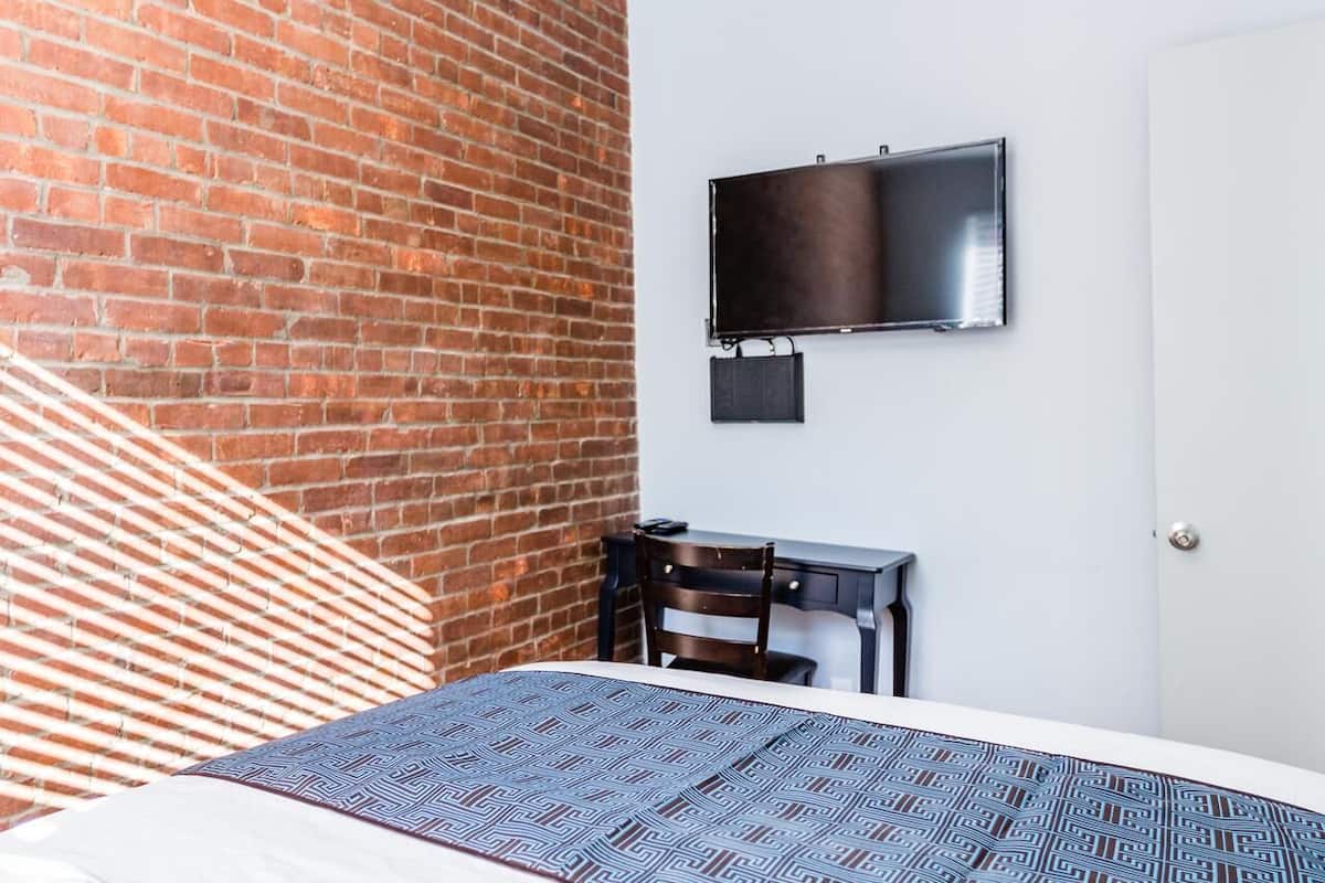 Een hotelkamer met een bakstenen muur, een bed met decoratieve beddengoed, een bureau met een stoel en een wandtelevisie.