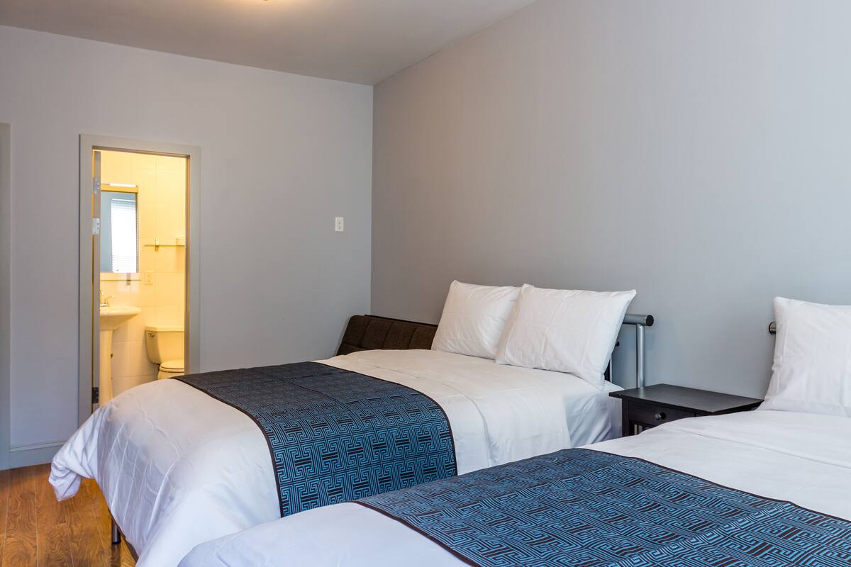 Een hotelkamer met twee bedden, een nachtkastje en een badkamer zichtbaar door een geopende deur.