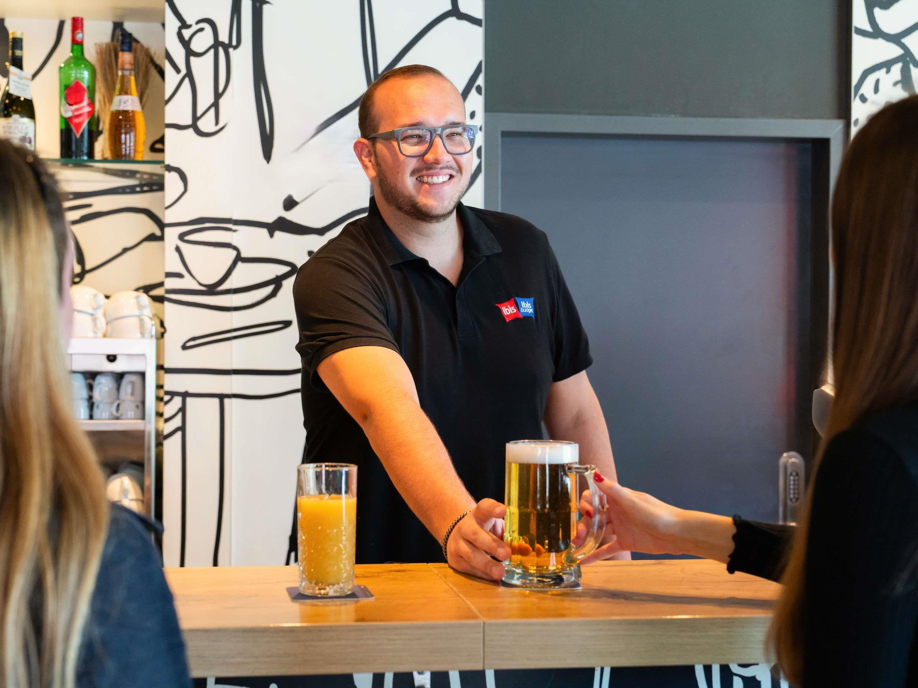 A person holding a beer mug at a bar with a glass of orange juice.