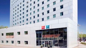Un moderno edificio de hotel con entrada de vidrio, un cartel de ibis budget y un cielo azul despejado.