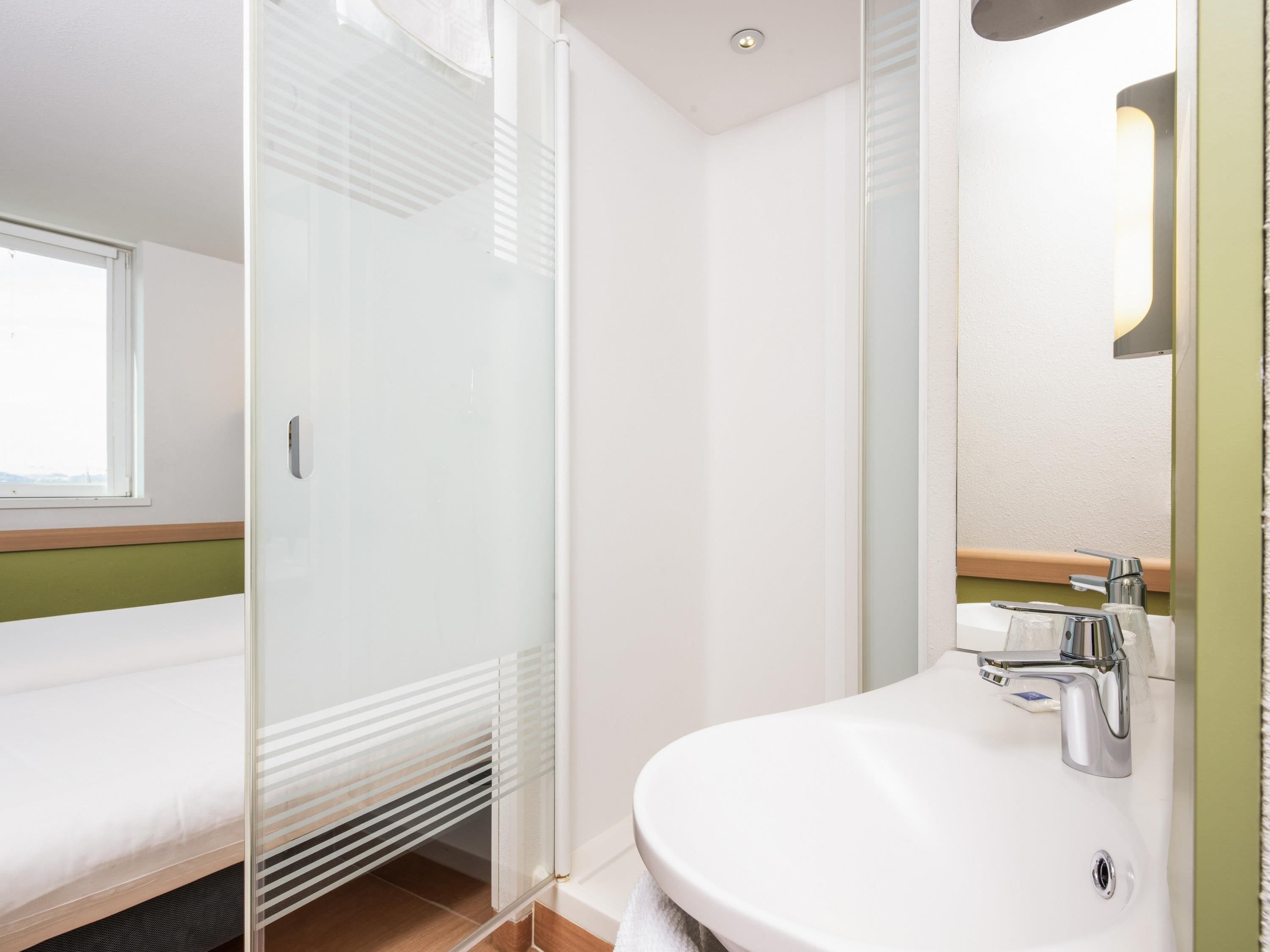Un baño moderno con cabina de ducha de vidrio, un lavabo blanco con grifo cromado y una pequeña ventana sobre la ducha.