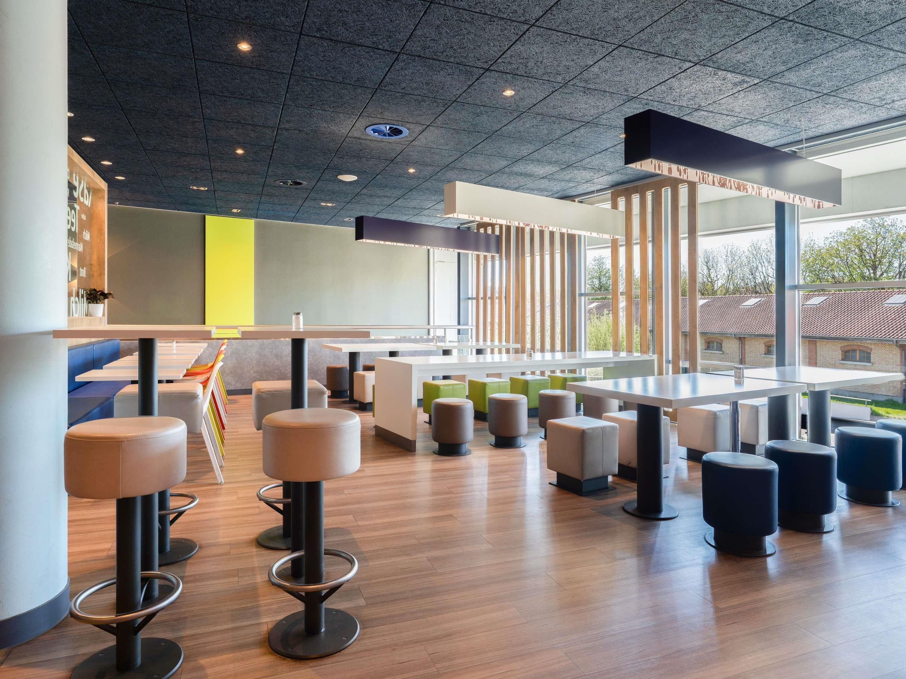 A modern interior with high ceilings, a mix of seating options including bar stools and cushioned chairs, and large windows offering views of the outside.