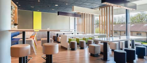 A modern interior with high ceilings, a mix of seating options including bar stools and cushioned chairs, and large windows offering views of the outside.