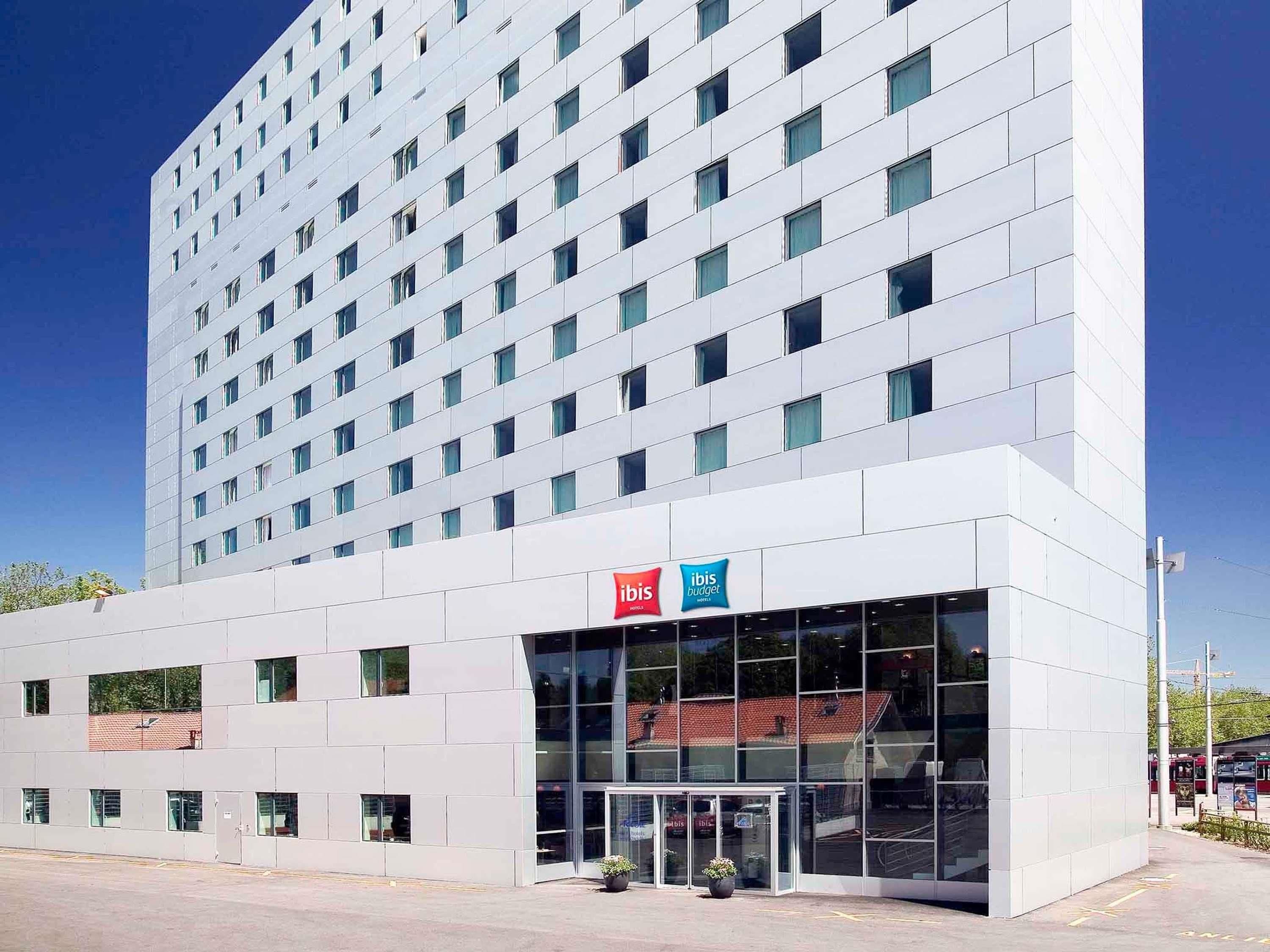 Un hôtel moderne avec une façade en verre, une enseigne « ibis budget » et un ciel d’un bleu éclatant.
