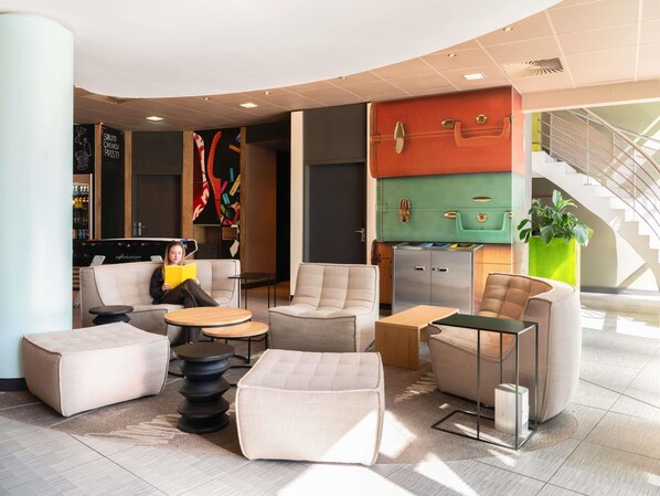A modern lounge area with sofas, ottomans, and a bar area with a colorful wall art. - ibis budget Bern Expo (Bern)