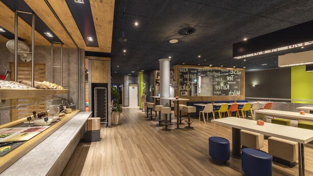 Un restaurante moderno con suelo de madera, una zona de buffet y un área de estar con sillas de colores.