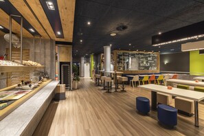 A modern restaurant with wooden flooring, a buffet area, and a seating area with colorful chairs. - ibis budget Bern Expo (Bern)