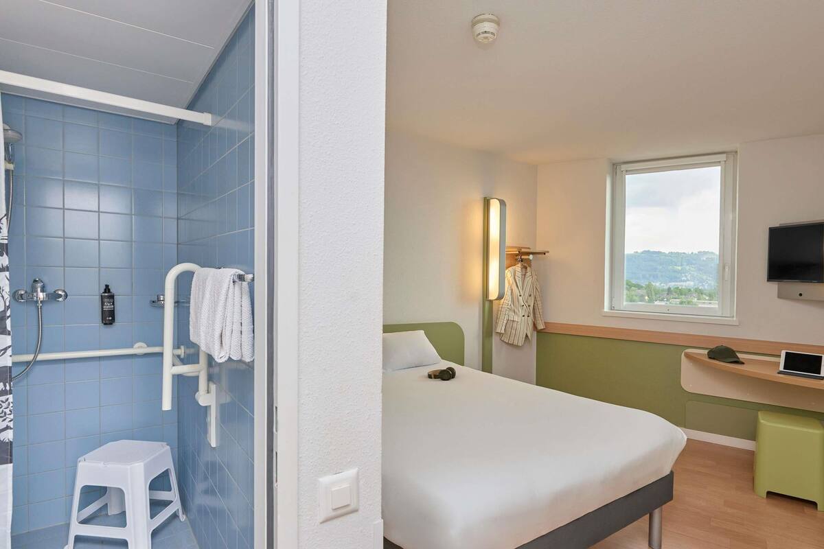 Una habitación de hotel con ducha, cama, escritorio y televisor.