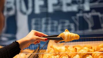 Una persona sosteniendo un croissant con unas pinzas sobre una bandeja de croissants.