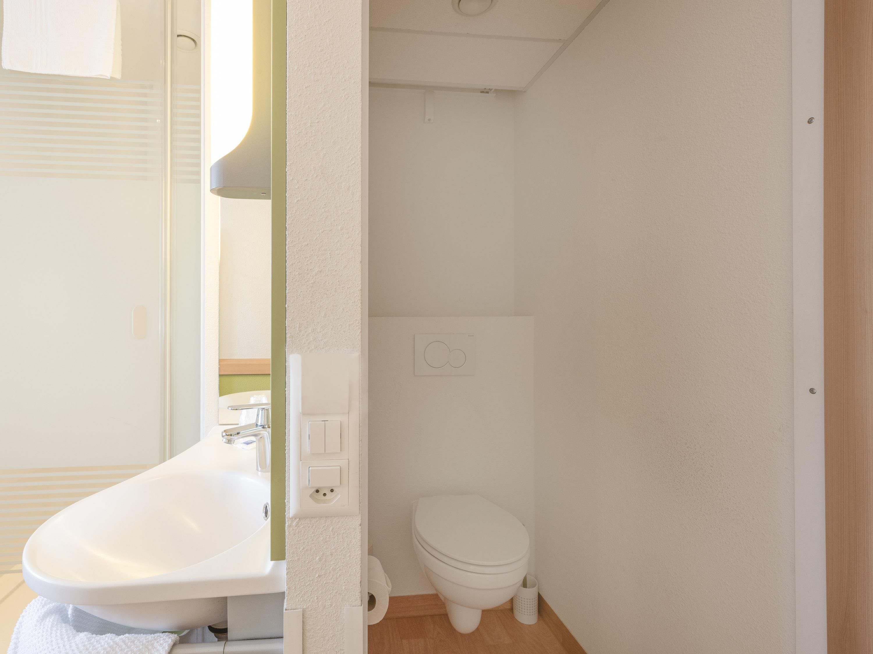 A small, clean bathroom with a sink, toilet, and a mirror.