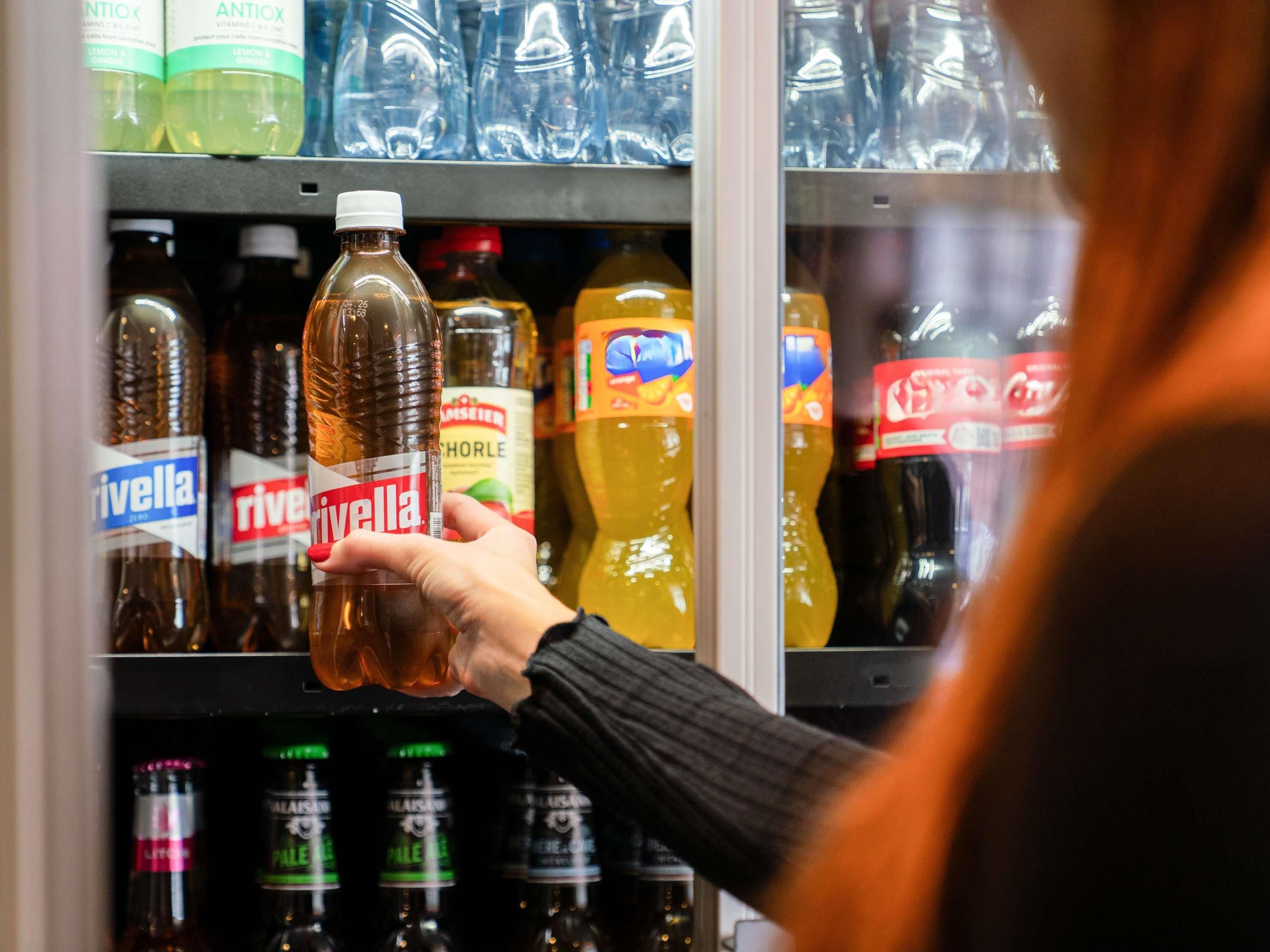 A hand holding a bottle of Antiox in a refrigerated display.