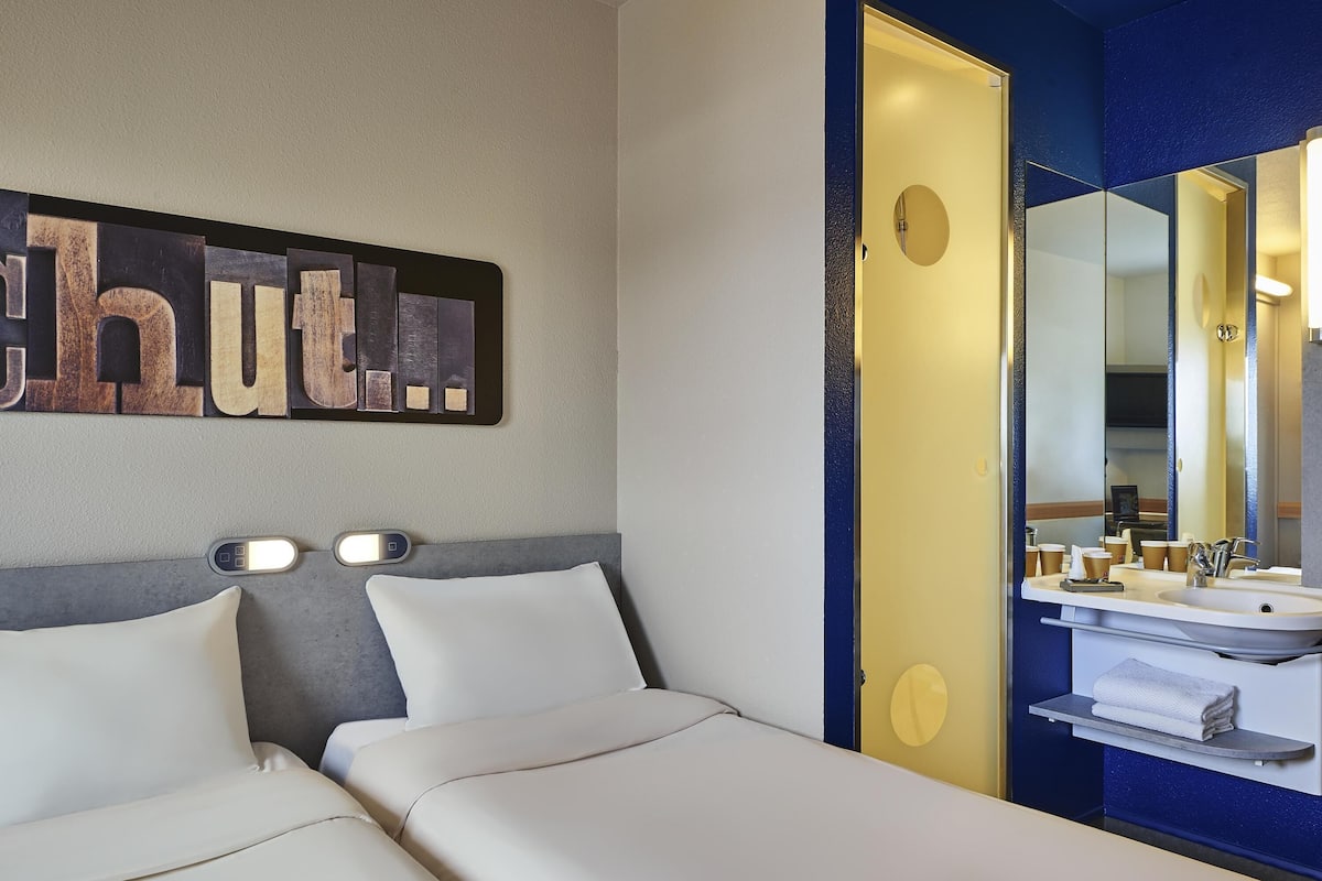 A hotel room with a bed, bedside tables, a mirror, a sink, and a towel rack.