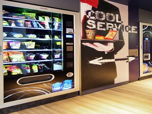 A vending machine with snacks and drinks, a wall with a 'COOL SERVICE' sign, and a hand pointing to an arrow. - ibis budget Vélizy (Velizy-Villacoublay)