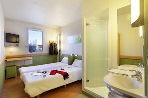 A hotel room with two beds, a bathroom with a sink and mirror, and a TV mounted on the wall. - ibis budget Vélizy (Velizy-Villacoublay)