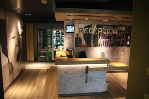 Mostrador de recepción con encimera de madera y zona de espera con televisor empotrado en la pared y un cartel.