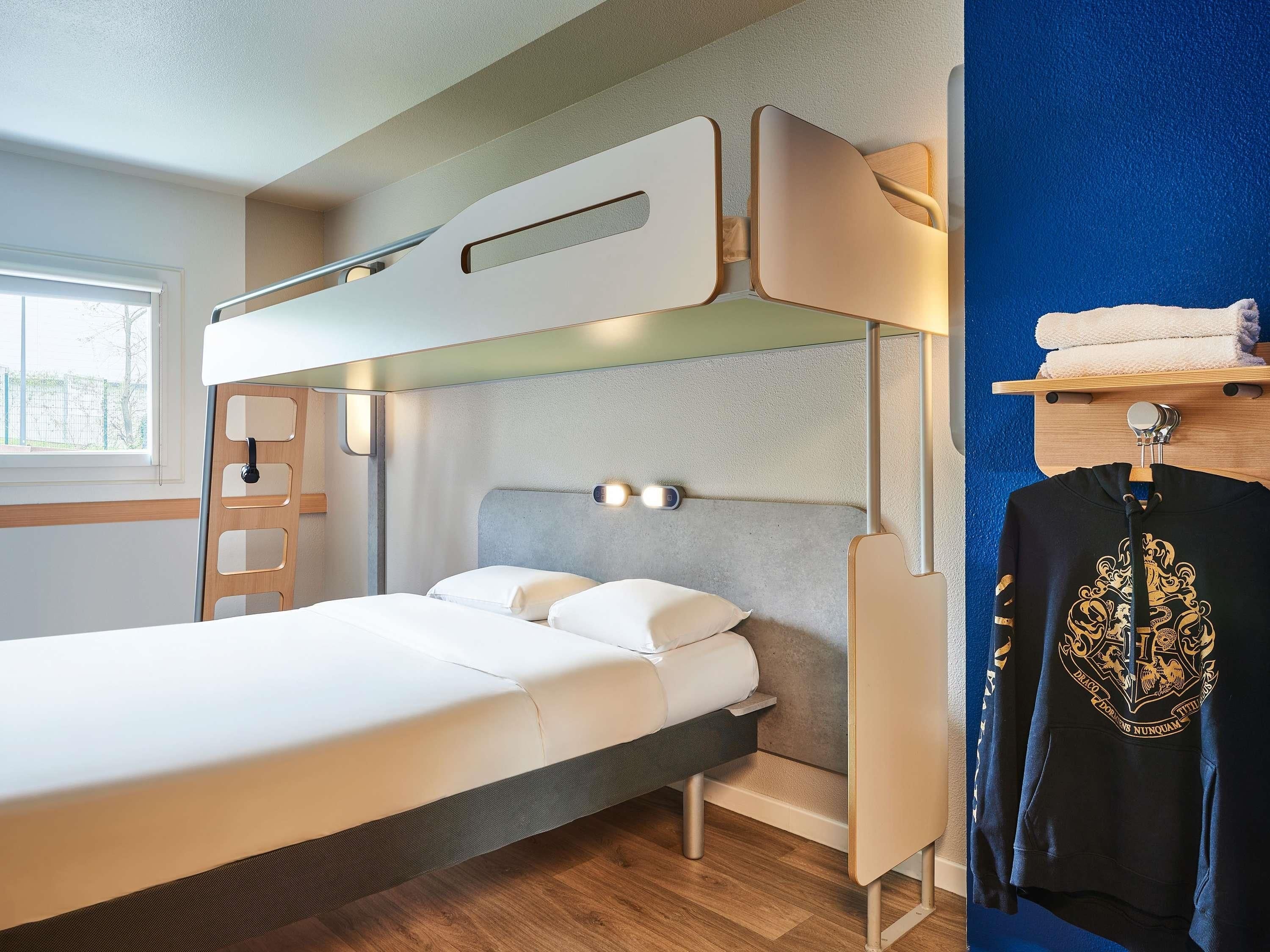 A bunk bed with a ladder, a bedside table, a wall-mounted light, and a window with a view.