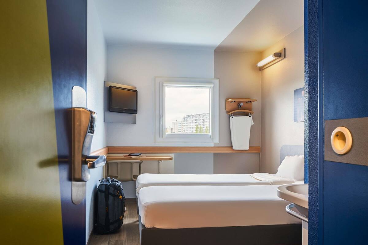 Pieni hotellihuone, jossa on sänky, pieni työpöytä, ikkuna ja kylpyhuone.
