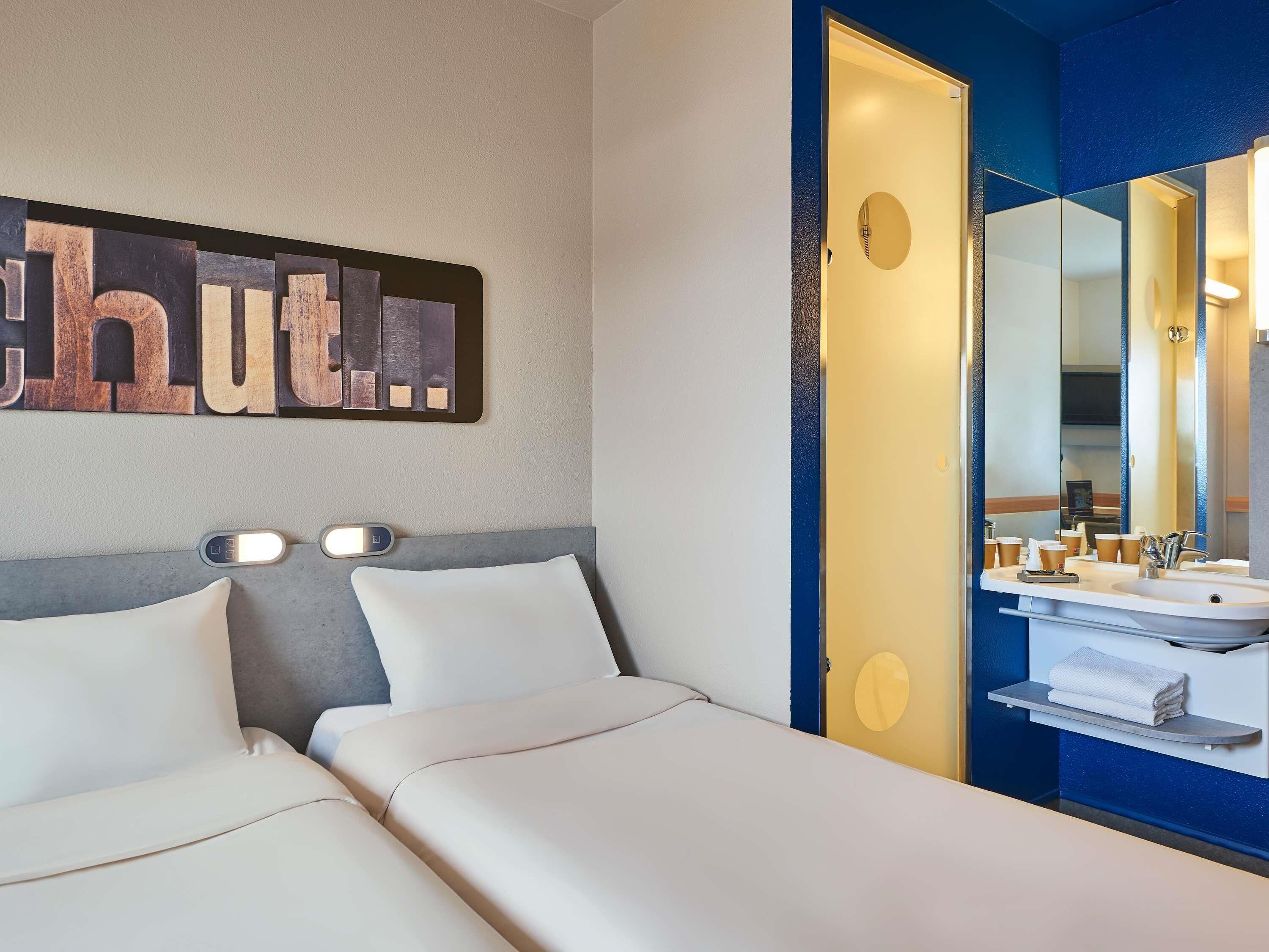 A hotel room with a bed, a wall-mounted artwork, a bathroom with a mirror, and a towel rack.