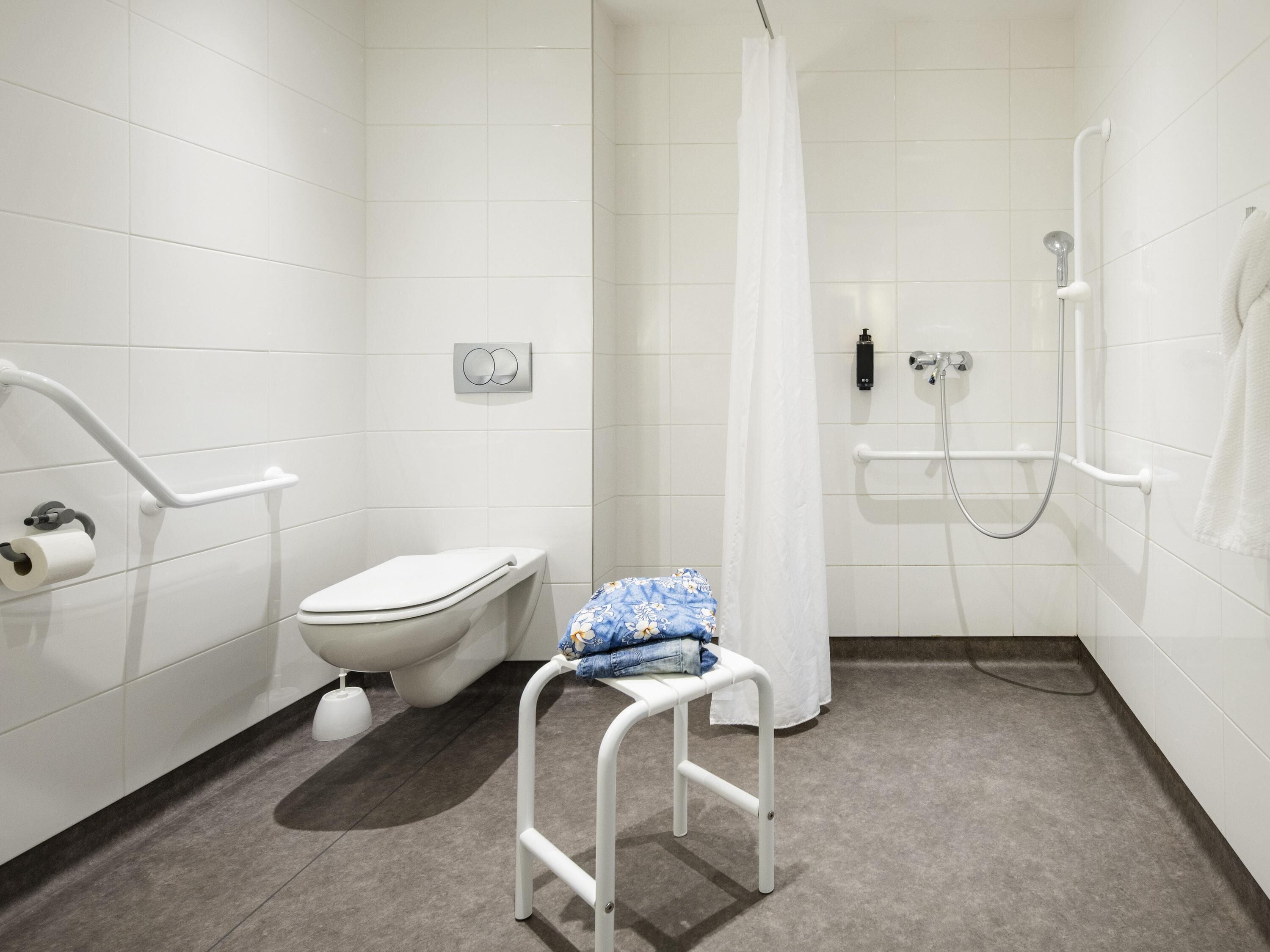 A modern bathroom with a toilet, a shower with a glass door, a white bench, and a towel rack.