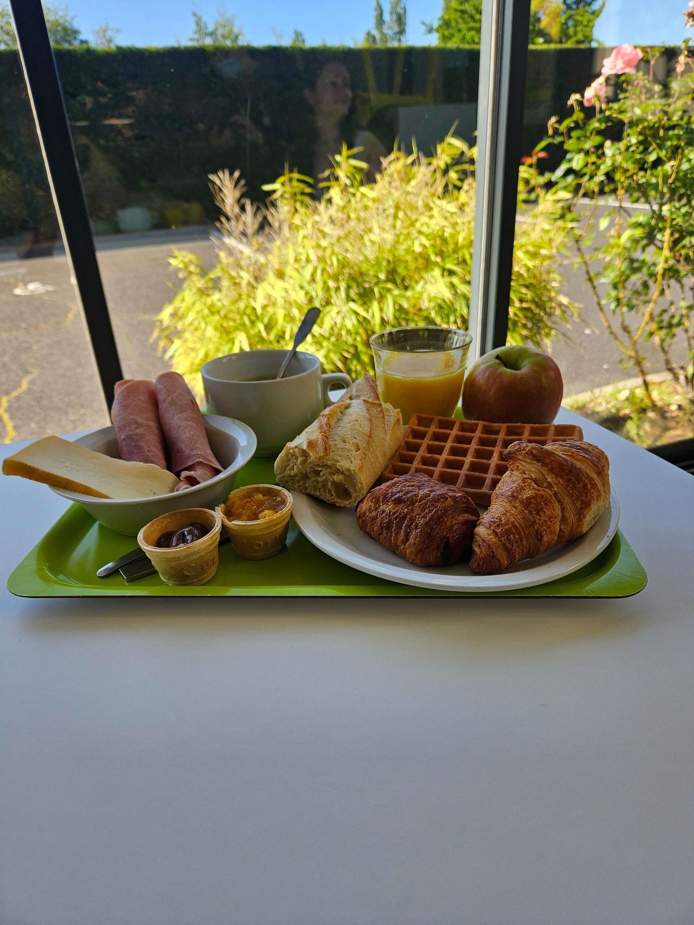 A breakfast tray with croissants, waffles, a bowl of ham, a cup of coffee, a glass of orange juice, and a small container of jam.