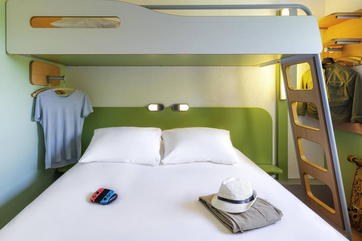 Uma cama beliche com cabeceira, uma mesa de cabeceira, uma luminária, uma toalha pendurada e um chapéu na cama.