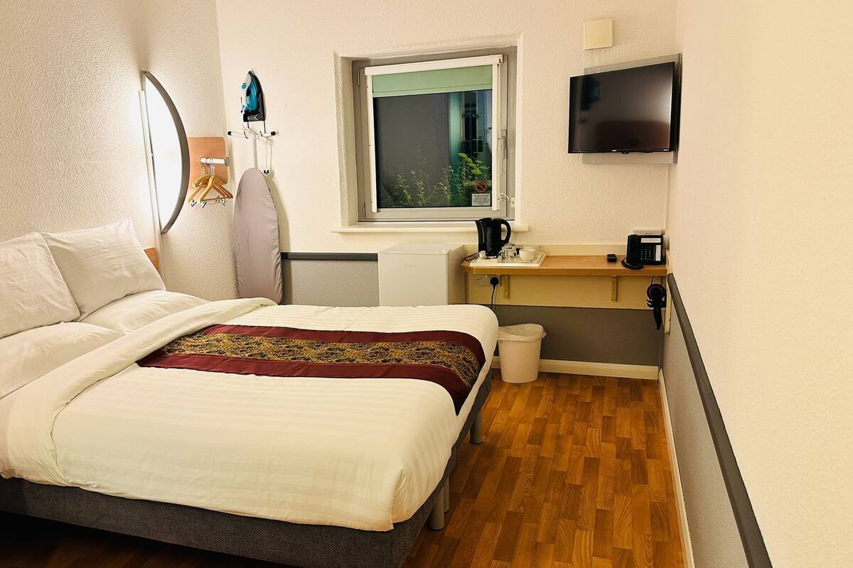 Habitación de hotel pequeña con cama, un escritorio con cafetera, televisor y ventana con vista.