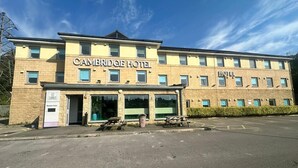 Un edificio con fachada de ladrillo, múltiples ventanas y un estacionamiento frente a él, identificado como el Hotel Cambridge.
